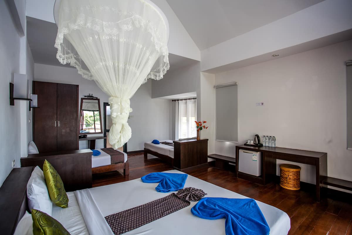 A hotel room with a large bed, a desk, a wardrobe, and a hanging canopy.