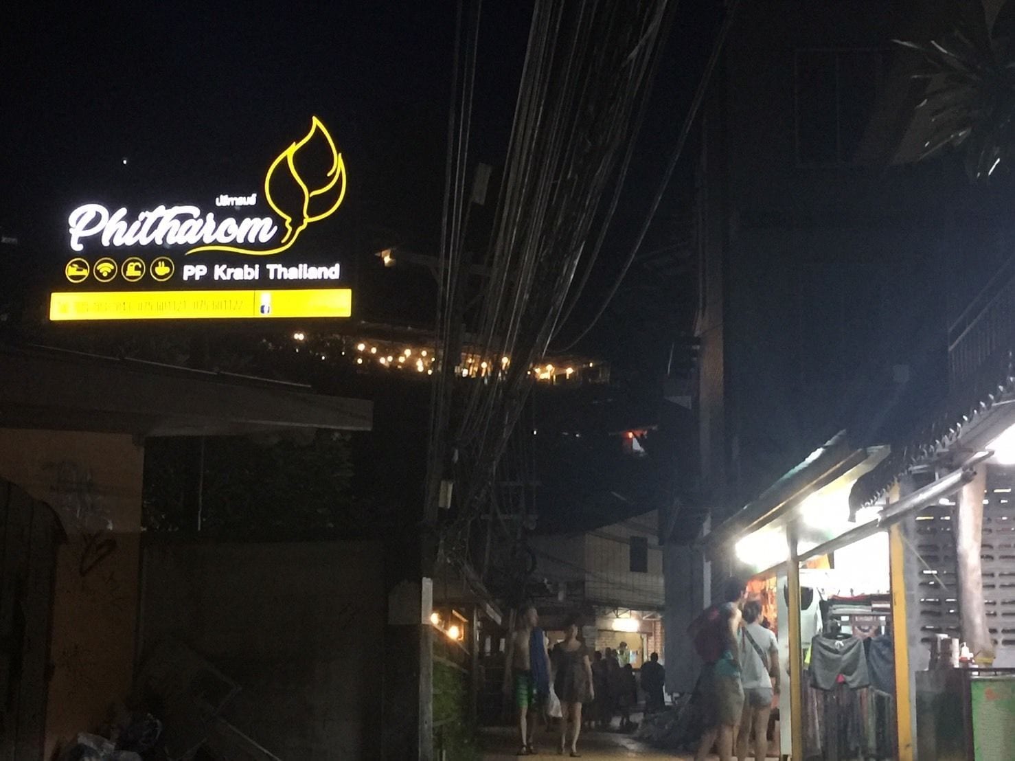 Et nattelivs billede af en gade med et neonskilt for 'Phitharom' og 'PP Krabi Thailand'.