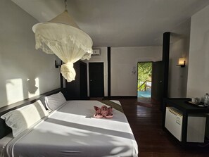 A hotel room with a bed, a desk, a chair, a nightstand, a bedside table, a lamp, and a window. - Phitharom PP Resort (Ko Phi Phi)