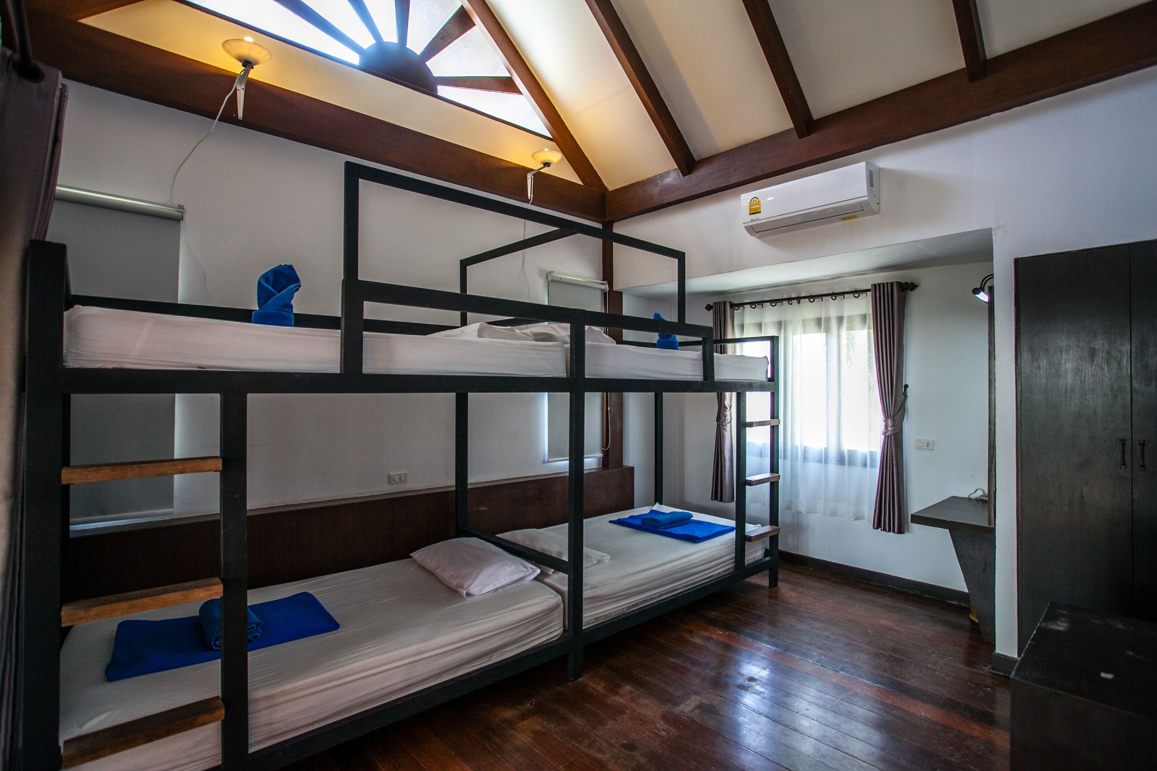 A bunk bed room with wooden beams, a skylight, and an air conditioning unit.