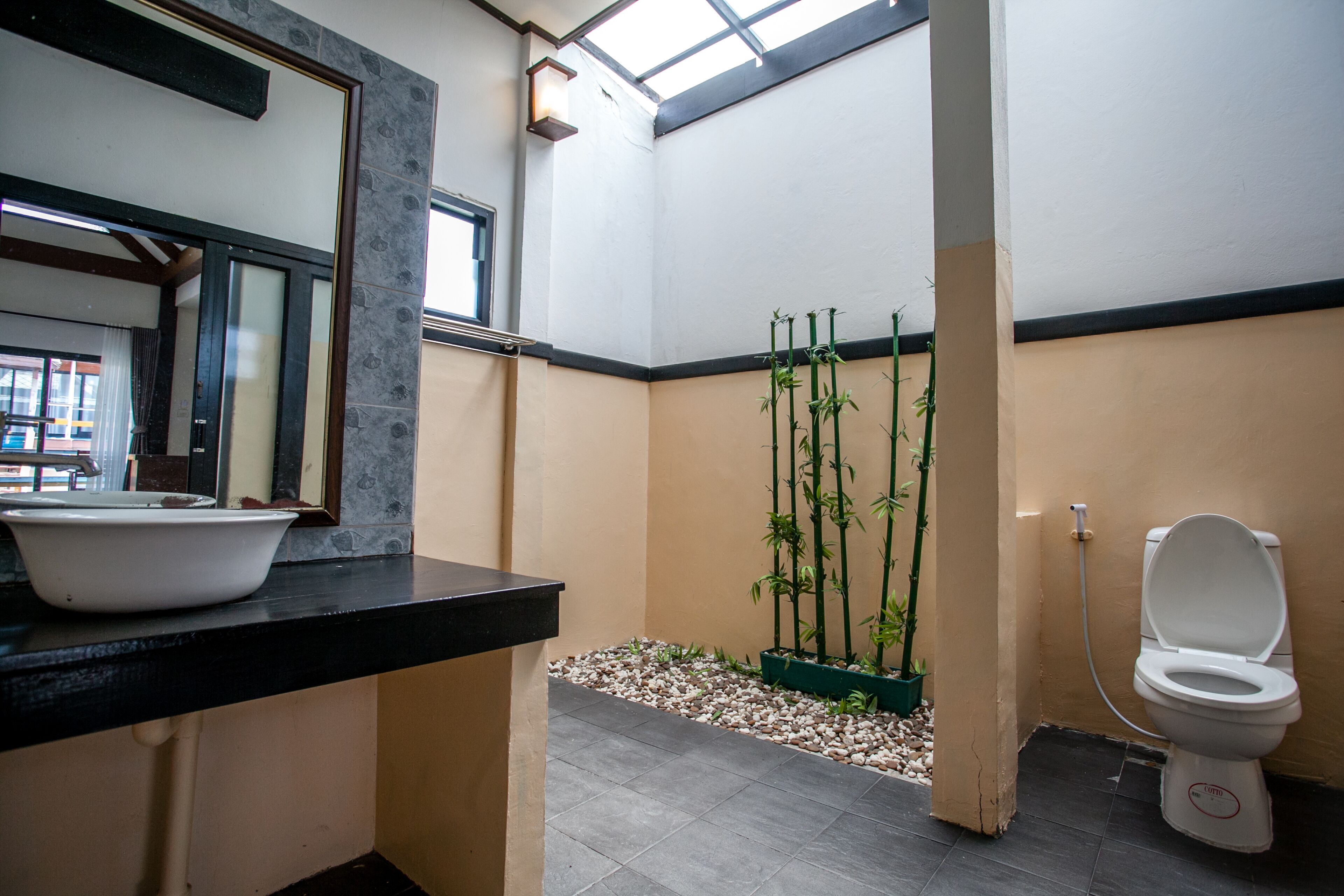 Une salle de bain avec un plan de toilette noir, un lavabo blanc, des toilettes et une plante en bambou dans un coin.