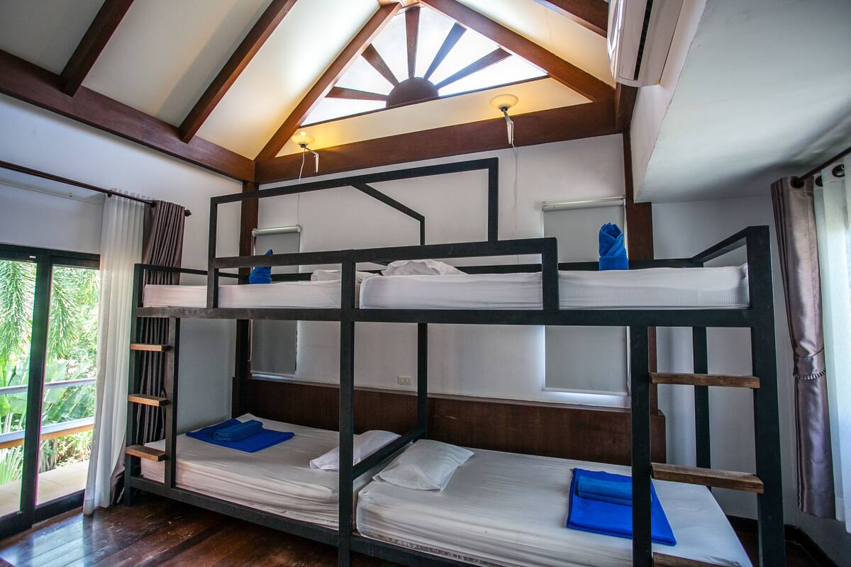 A bunk bed room with a skylight, wooden beams, and a view of greenery outside.
