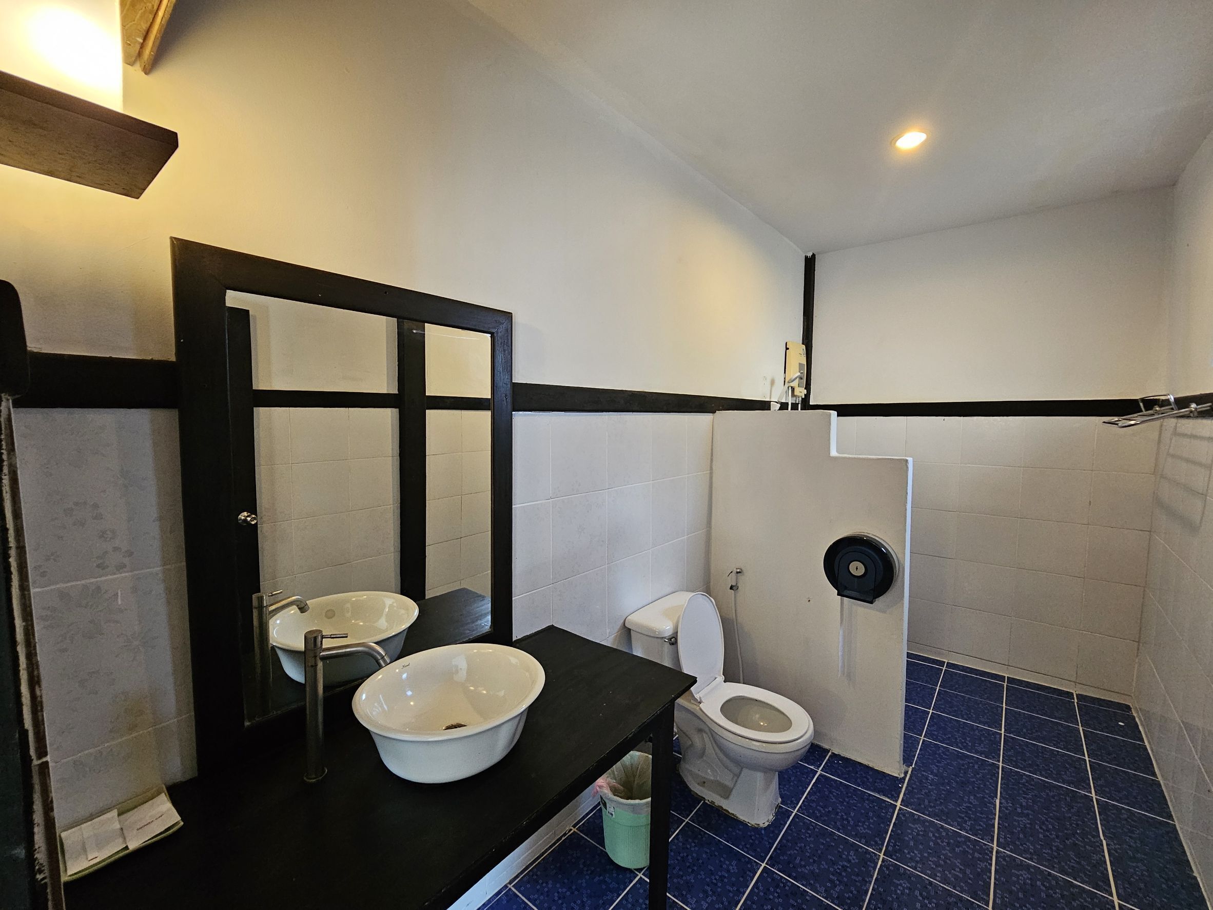 Ein Badezimmer mit schwarzer Ablage, weißem Waschbecken, einem Spiegel, einer Toilette und einem blau gefliesten Boden.