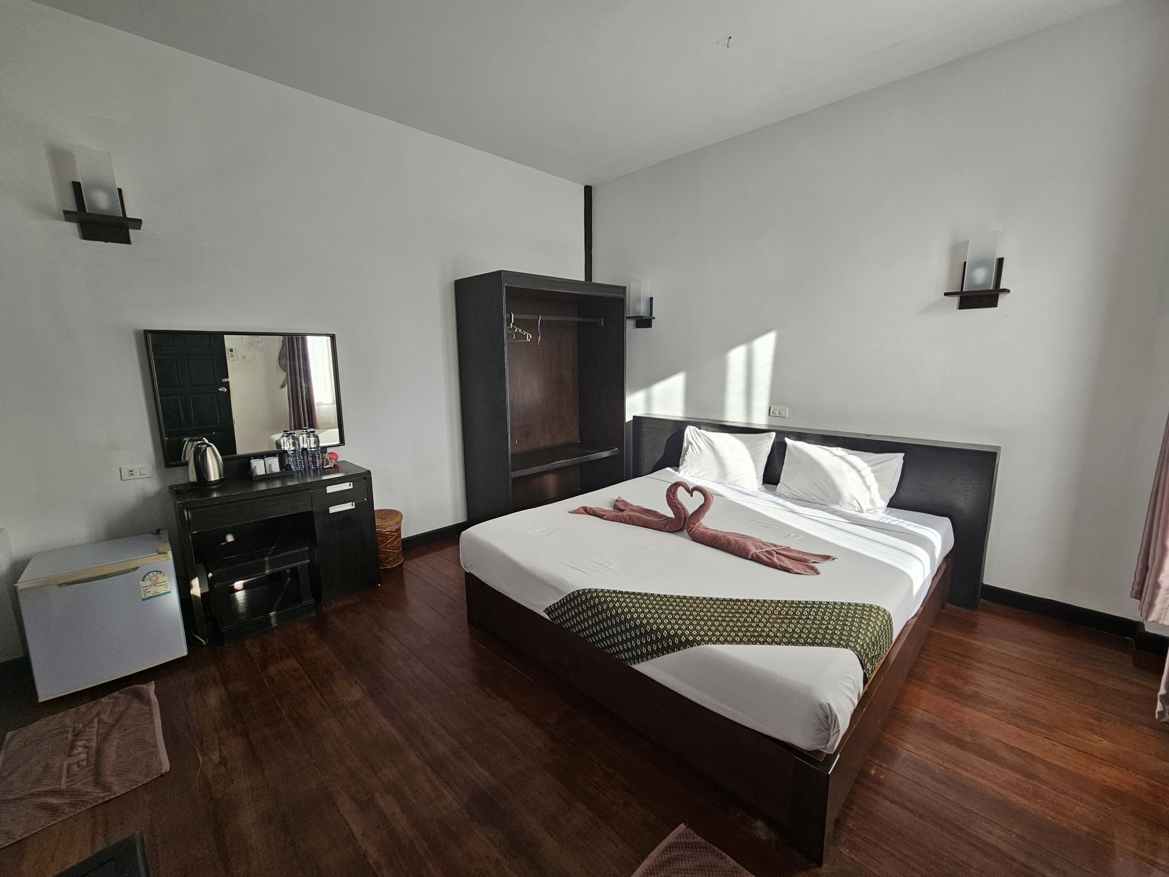 Habitación de hotel con una cama grande, un armario, un escritorio con espejo y un pequeño cubo de basura.