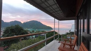 A balcony with wooden chairs, overlooking a coastal view with mountains and a body of water.