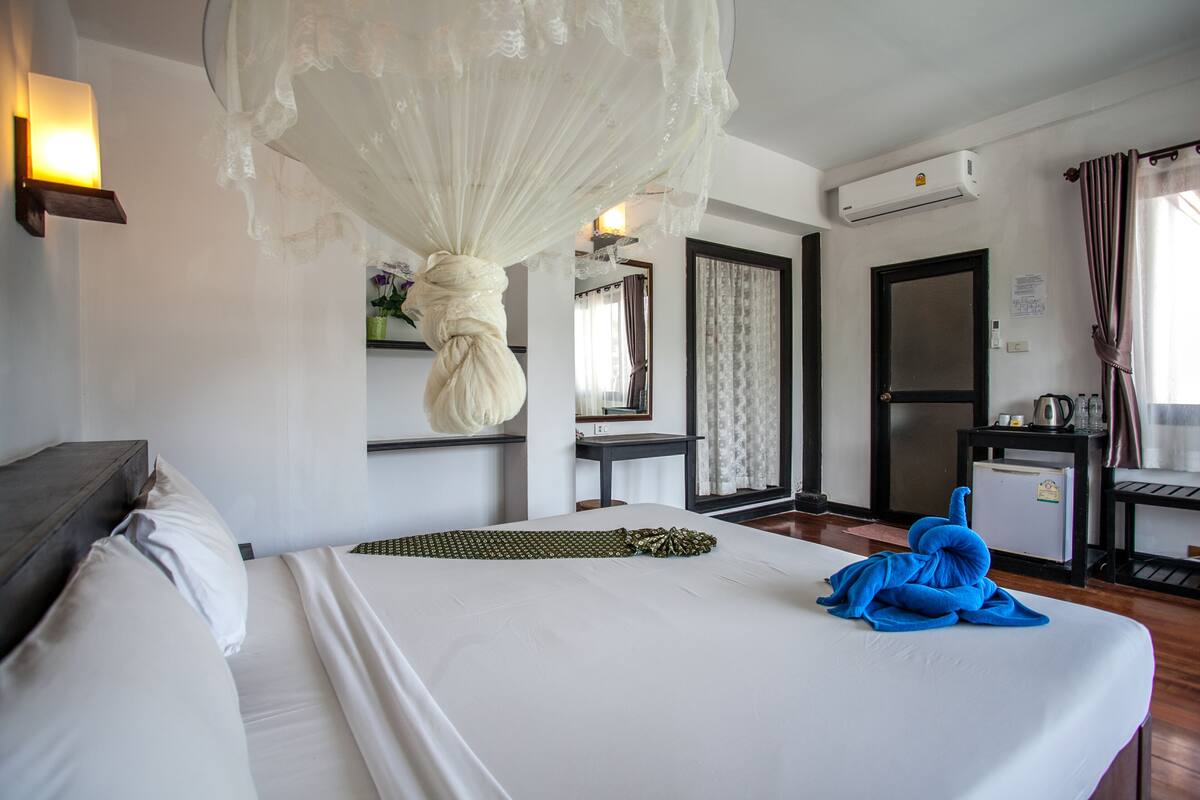A hotel room with a bed, a bedside table, a mirror, a wardrobe, and an air conditioning unit.