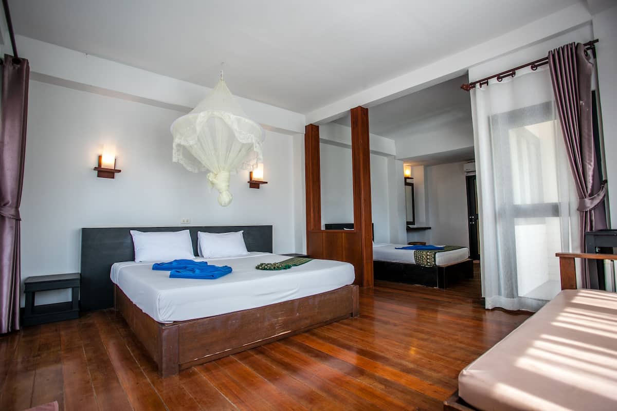 A hotel room with a large bed, a nightstand, a bedside table, a mirror, and a chandelier.