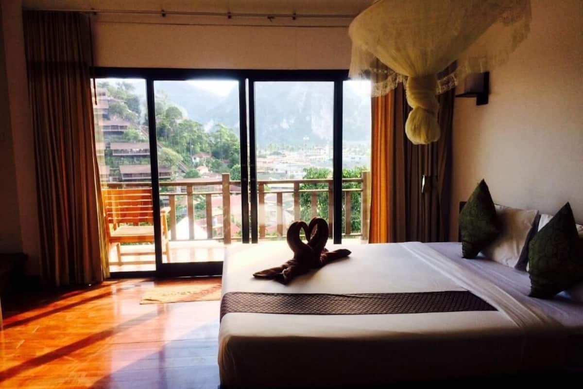 A hotel room with a bed, a large window with a view of a mountainous landscape, and a balcony.