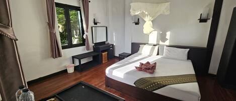 Una habitación de hotel con cama, mesita de noche, banco, ventana con cortinas y lámpara colgante.