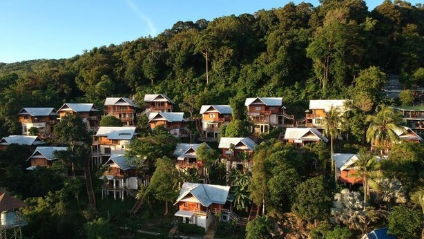 A hillside resort with multiple wooden chalets, a swimming pool, and lush greenery.