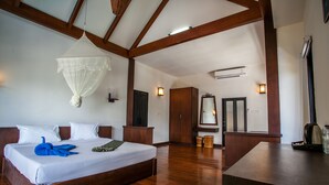 A spacious bedroom with a large bed, wooden beams, a hanging mosquito net, and a wooden dresser.