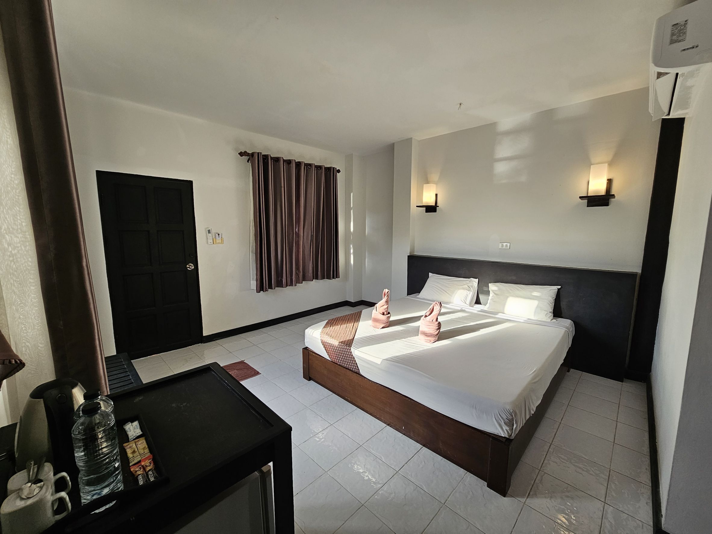 A hotel room with a bed, bedside tables, a desk, a water bottle, and a coffee maker.