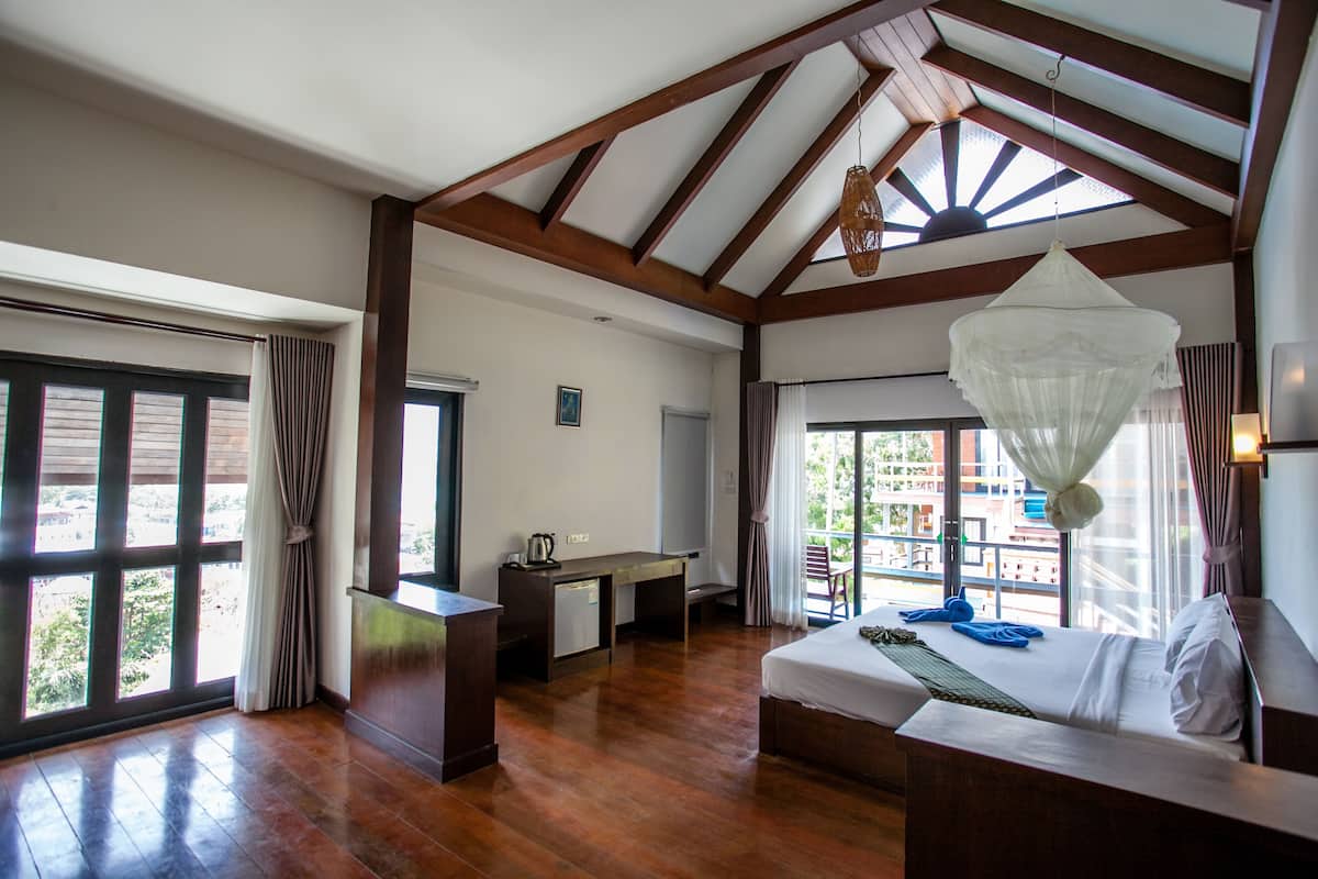 A hotel room with a large bed, a desk, and a balcony with a view.