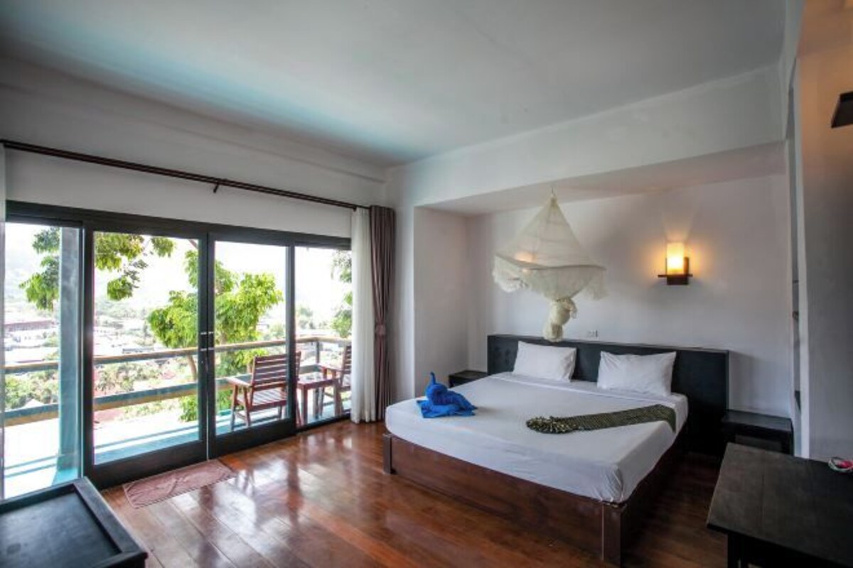 A hotel room with a large bed, a desk, and a balcony with a chair.
