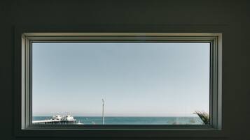 A window with a view of the ocean, a pier, and a lighthouse.