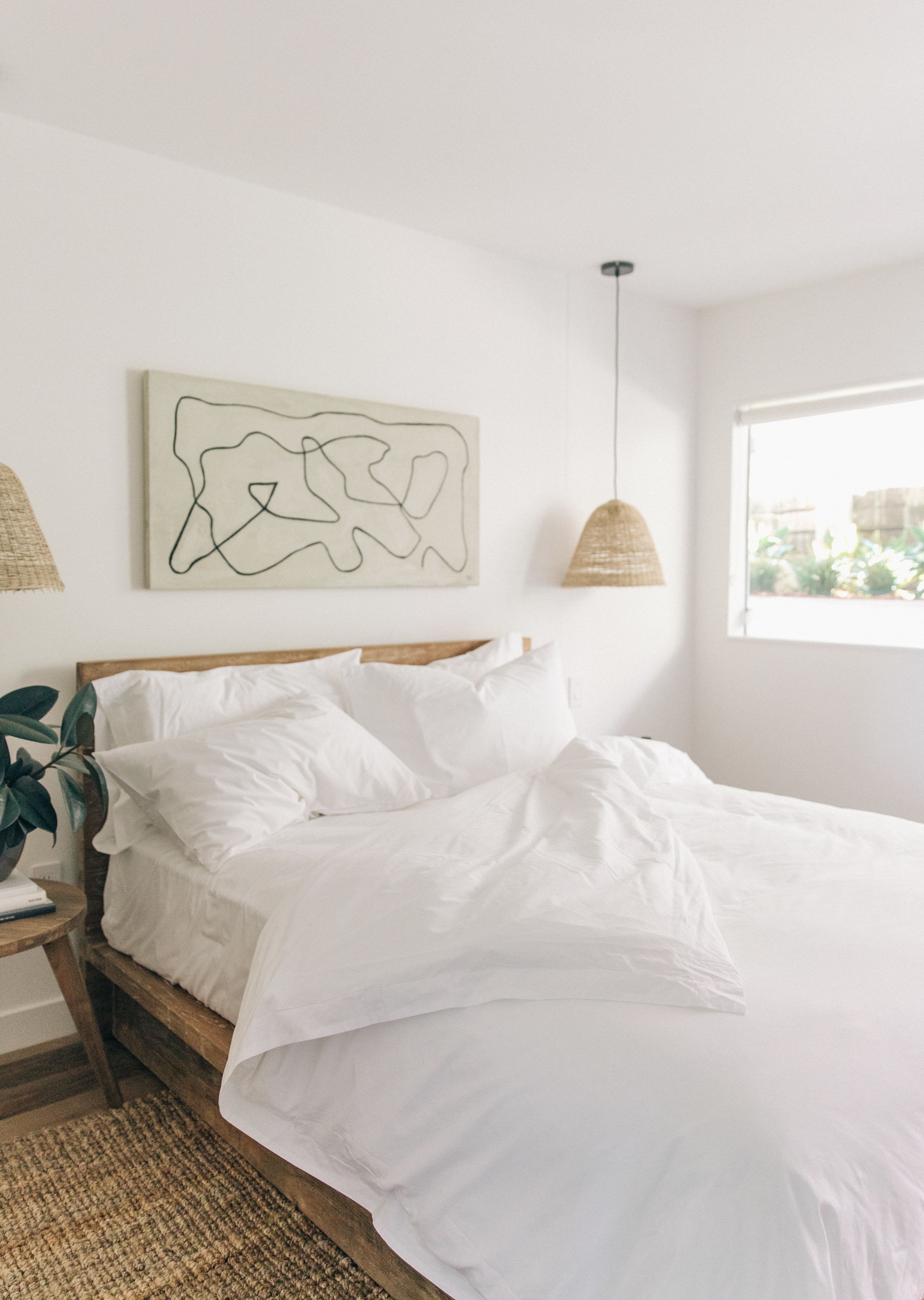 A bedroom with a bed, a hanging lamp, a wall art piece, and a window.