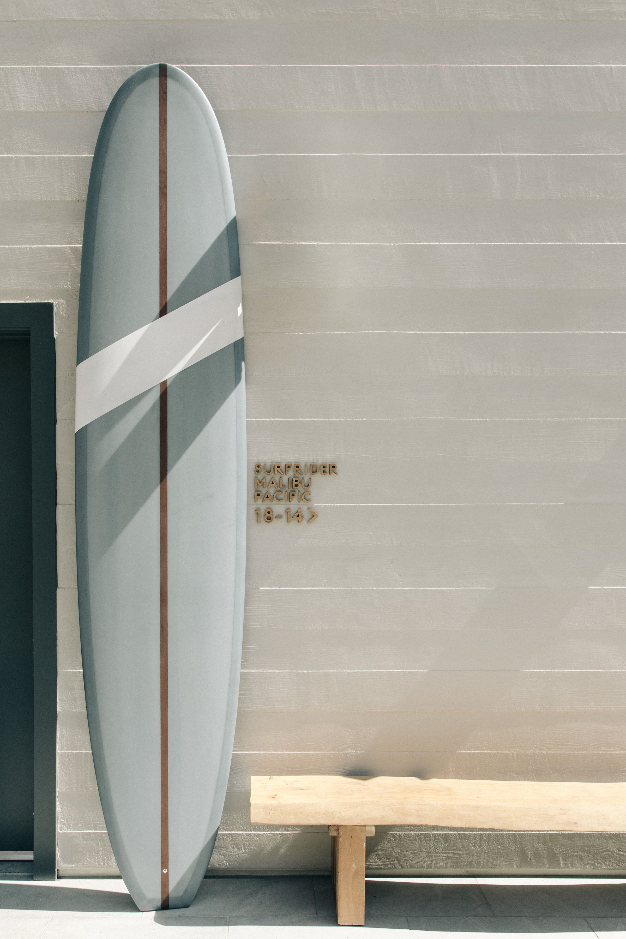 A surfboard leaning against a wall with a bench nearby.