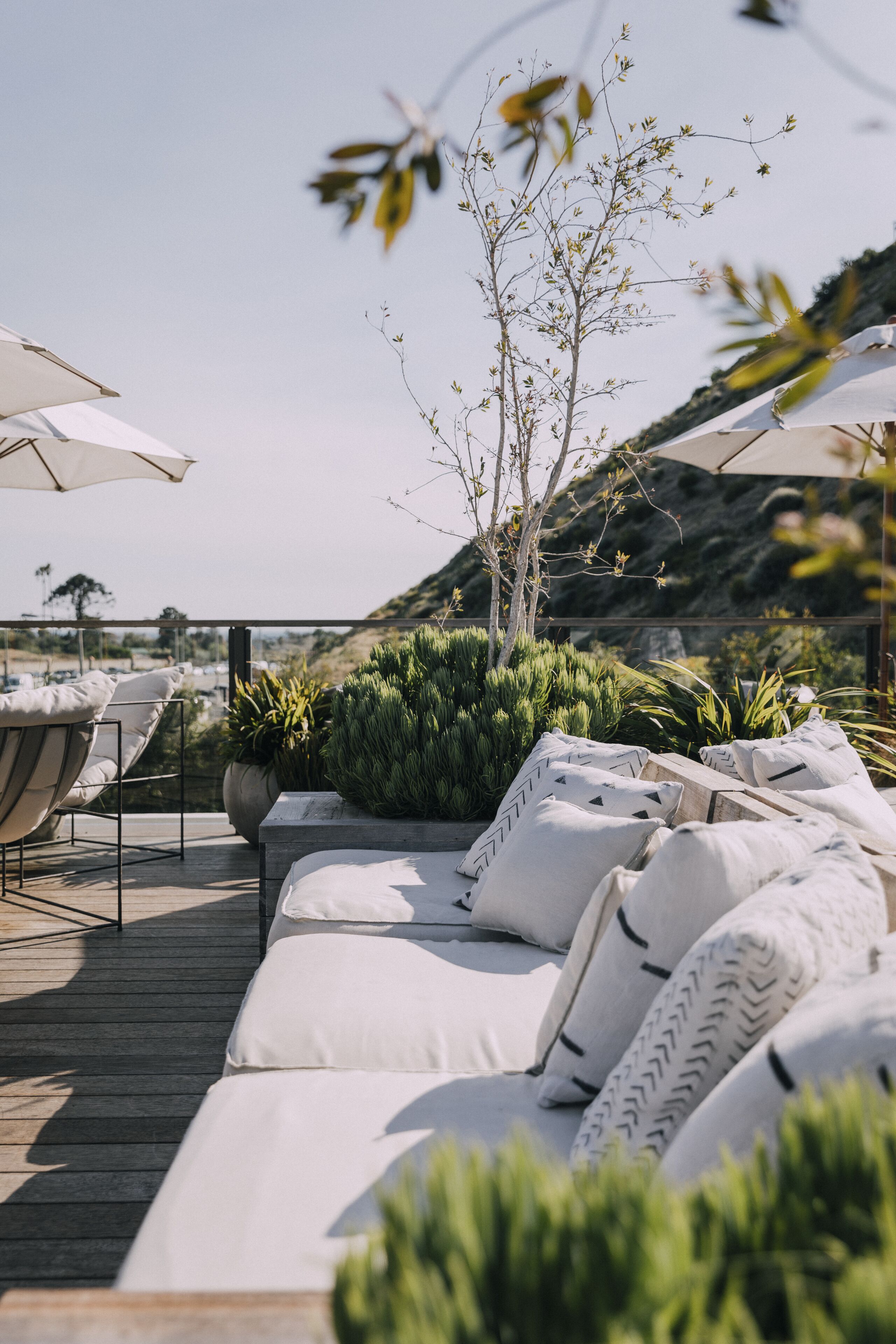 Terraza con sillones de descanso y sombrillas, rodeada de vegetación y vistas al paisaje.