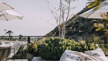 Terraza con sillones de descanso y sombrillas, rodeada de vegetación y vistas al paisaje.