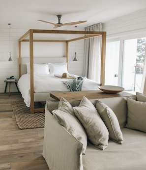 A bedroom with a four-poster bed, a wooden coffee table, a sofa, and a large window.