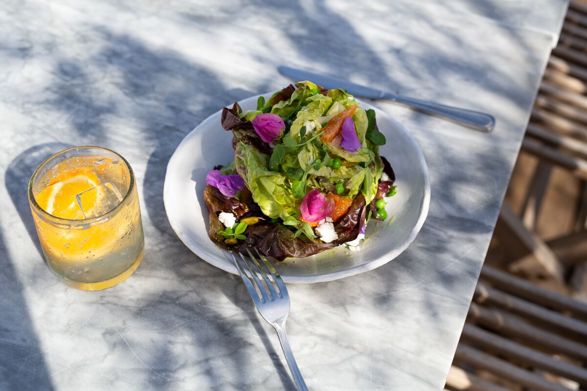 Une assiette de salade, une fourchette et un verre de jus d’orange sont posés sur une table en marbre.