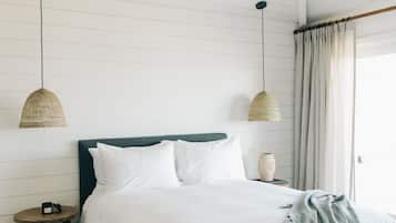 A bedroom with a bed, a ceiling fan, pendant lights, a bedside table, and a window with curtains.