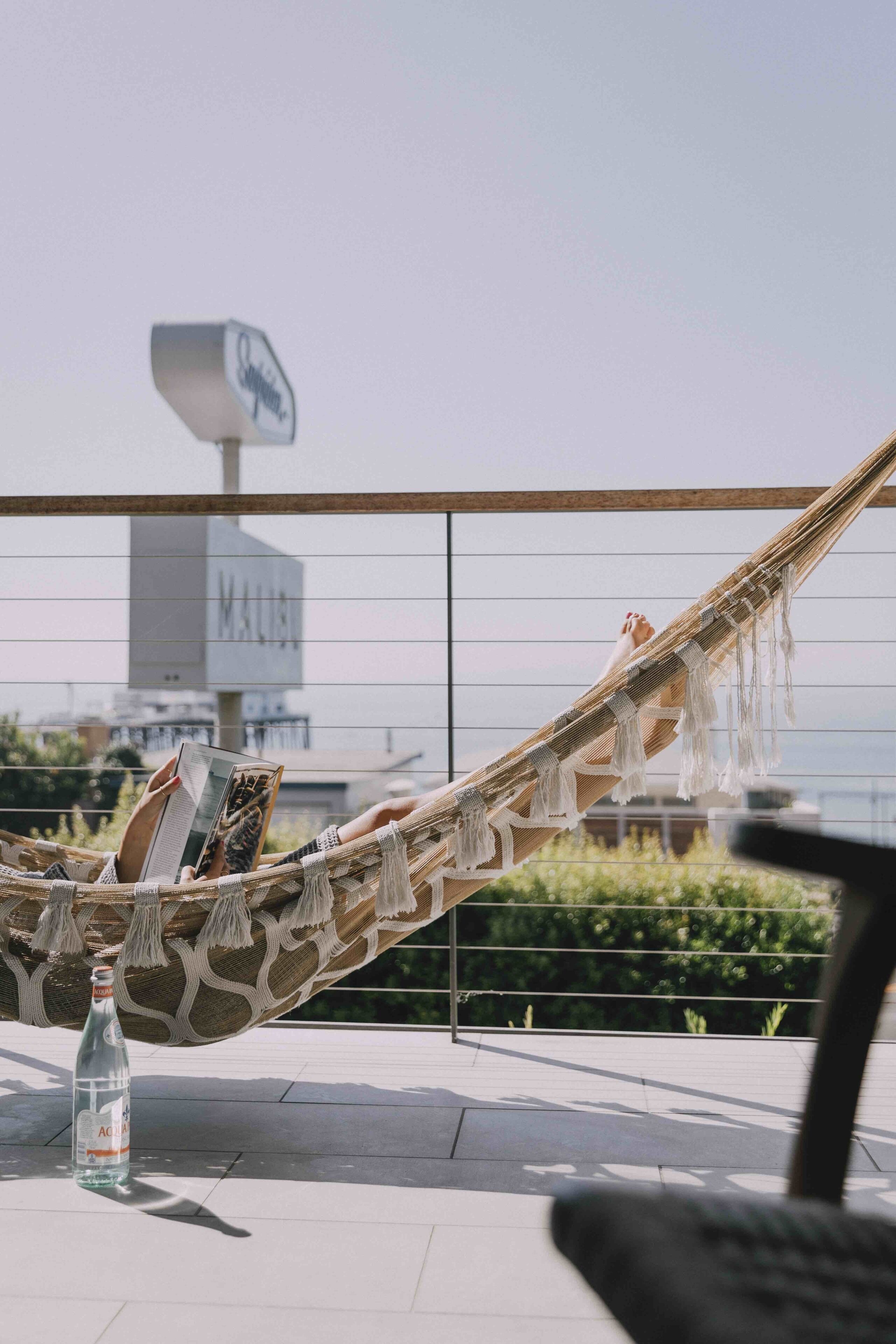 A hammock with a person reading a book, a bottle of water, and a view of a building with a sign.
