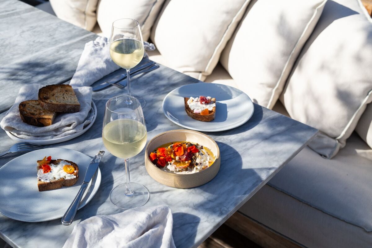 Una mesa servida con platos de comida, una copa de vino blanco y cubiertos.