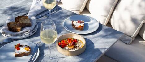 Una mesa servida con platos de comida, una copa de vino blanco y cubiertos.