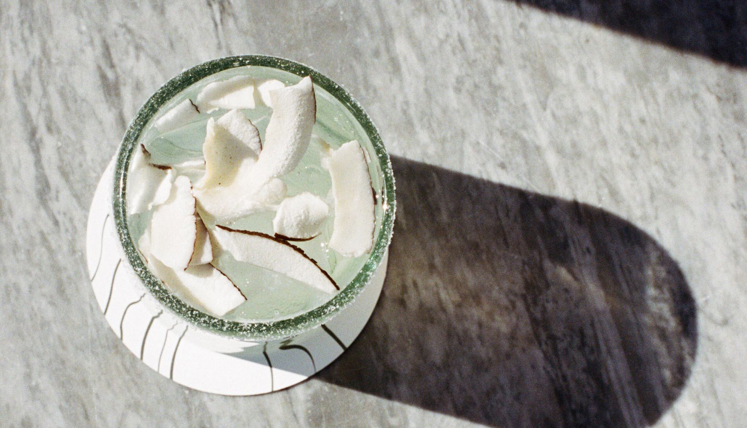 A glass with a green rim and a white base, containing a clear liquid and white spherical objects, possibly ice, on a marble surface.