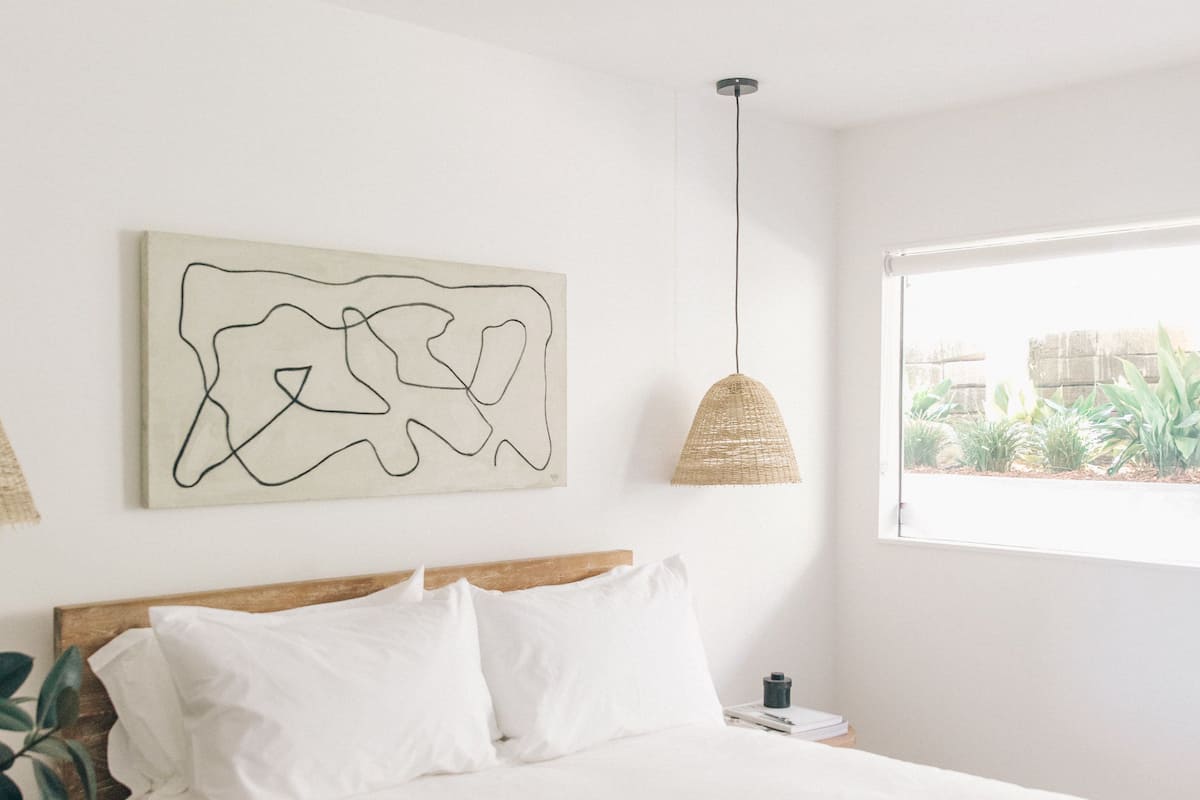 Ein Schlafzimmer mit einem großen Bett, einer Hängelampe, einem Fenster mit Blick auf Grünflächen und einem Wandbild.