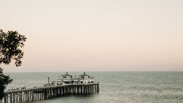 A pier extending into calm water with a building featuring multiple levels and a dome-like structure at the end.