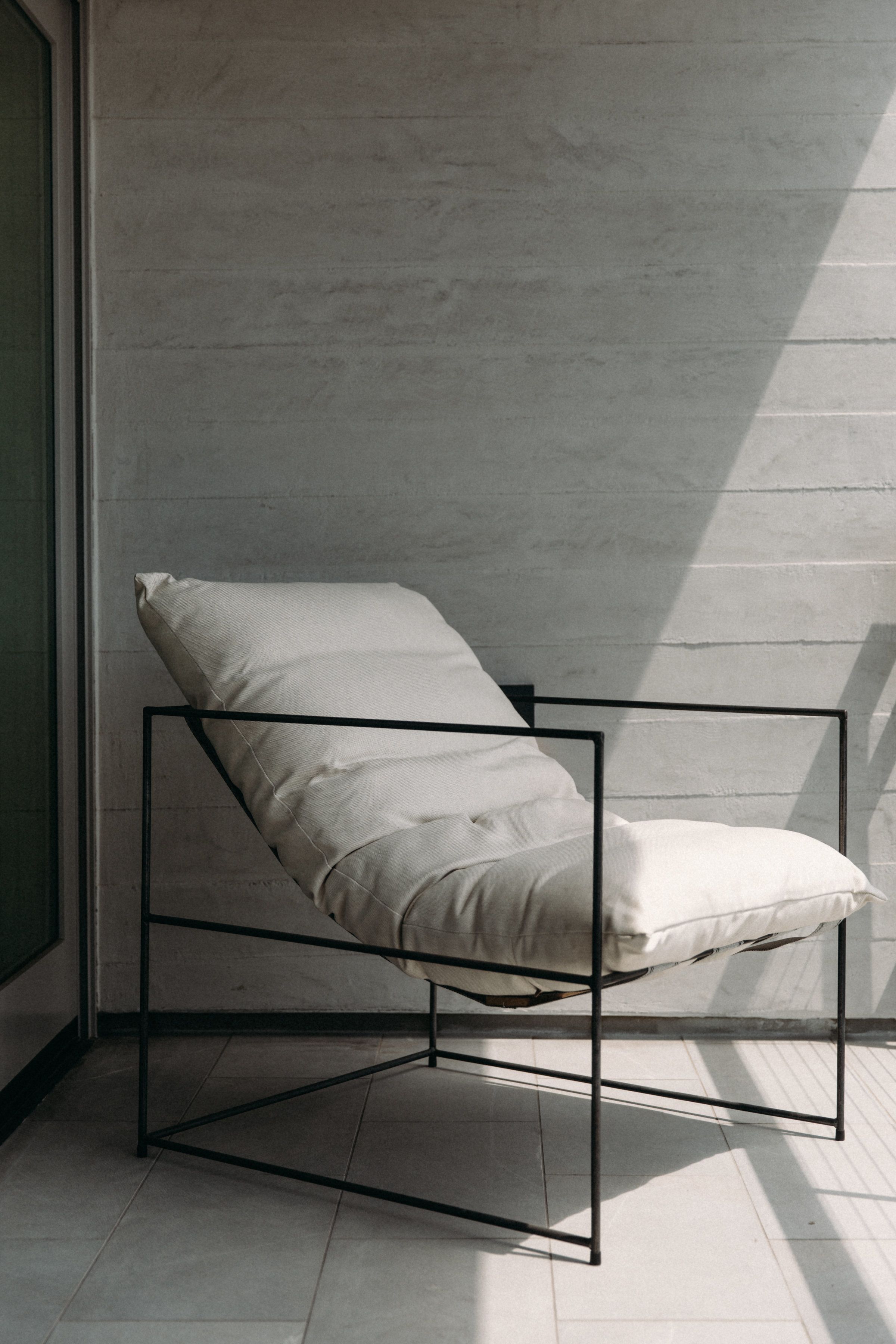 A modern chair with a metal frame and a cushion, positioned against a plain wall with a shadow cast on it.