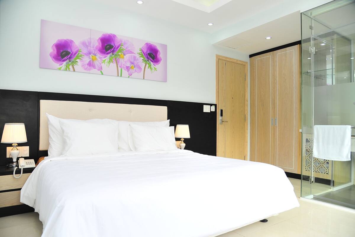Une chambre d’hôtel avec un grand lit, deux lampes de chevet, une armoire en bois et une cabine de douche en verre.