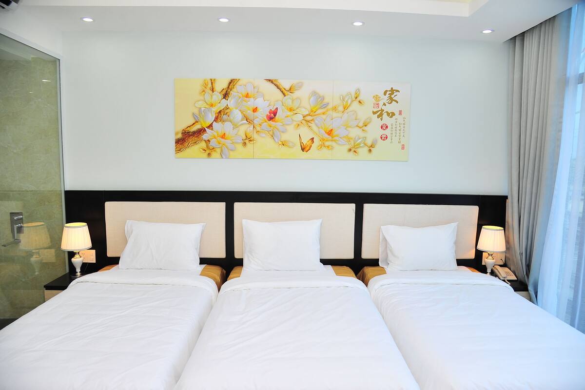 Une chambre d’hôtel avec un grand lit, deux tables de chevet avec des lampes, une œuvre d’art accrochée au mur et une cloison en verre.