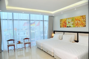 A hotel room with a large bed, two bedside tables, a small table with chairs, and a large window with curtains. - Golden Dragon Hotel (Gia Tran)