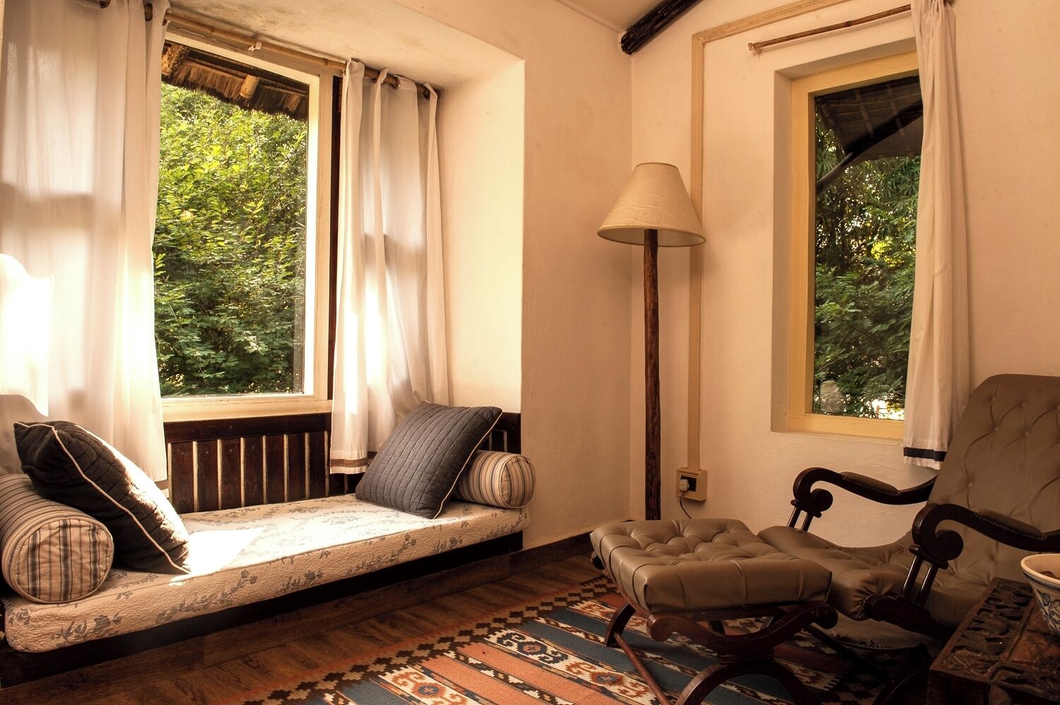 A cozy room with a cushioned bench, a wooden chair, a floor lamp, and a patterned rug.