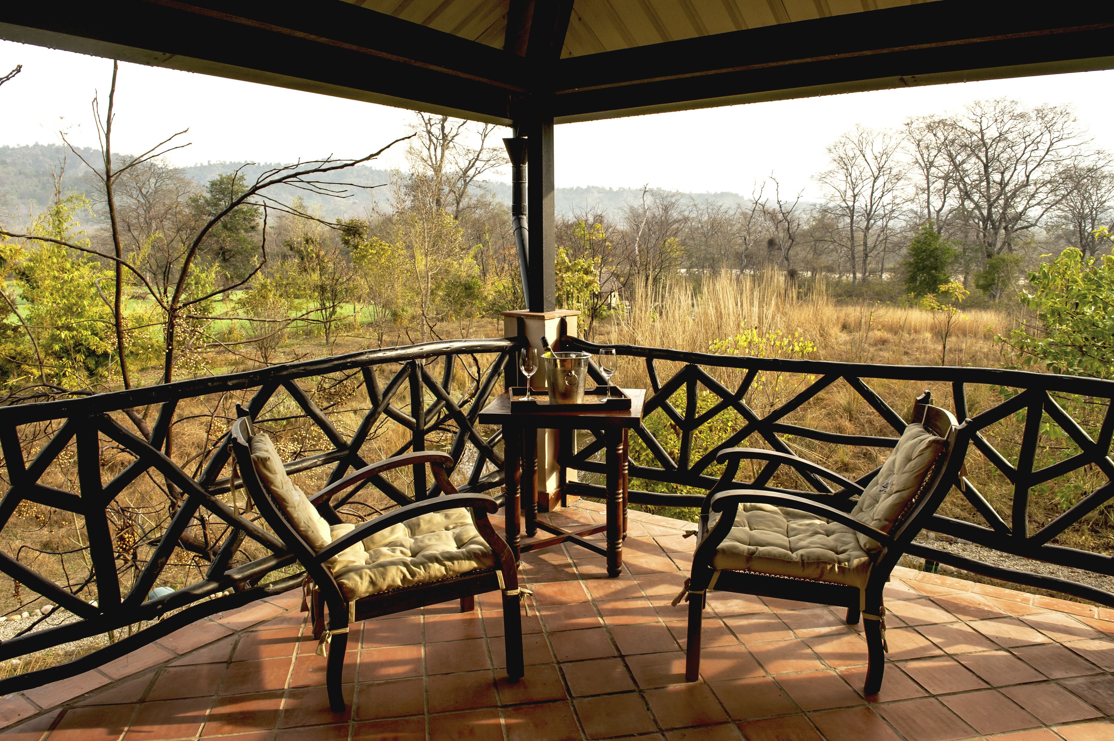 Un espacio al aire libre techado con dos sillas y una mesa, con vista a un paisaje natural con árboles y colinas.