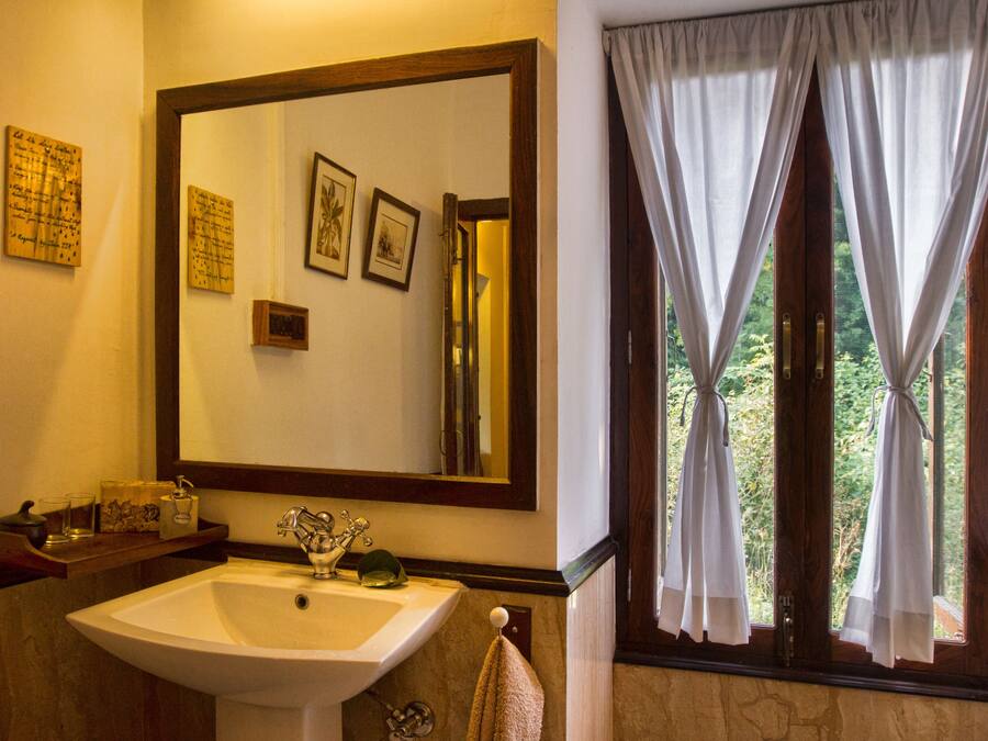 Un baño con un espejo grande, un lavamanos y una ventana con cortinas.