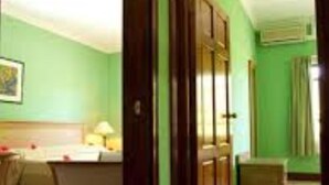 A hotel room with a bed, a desk, and a chair. There is a door leading to another room. - Gregoire's Apartments (La Digue)