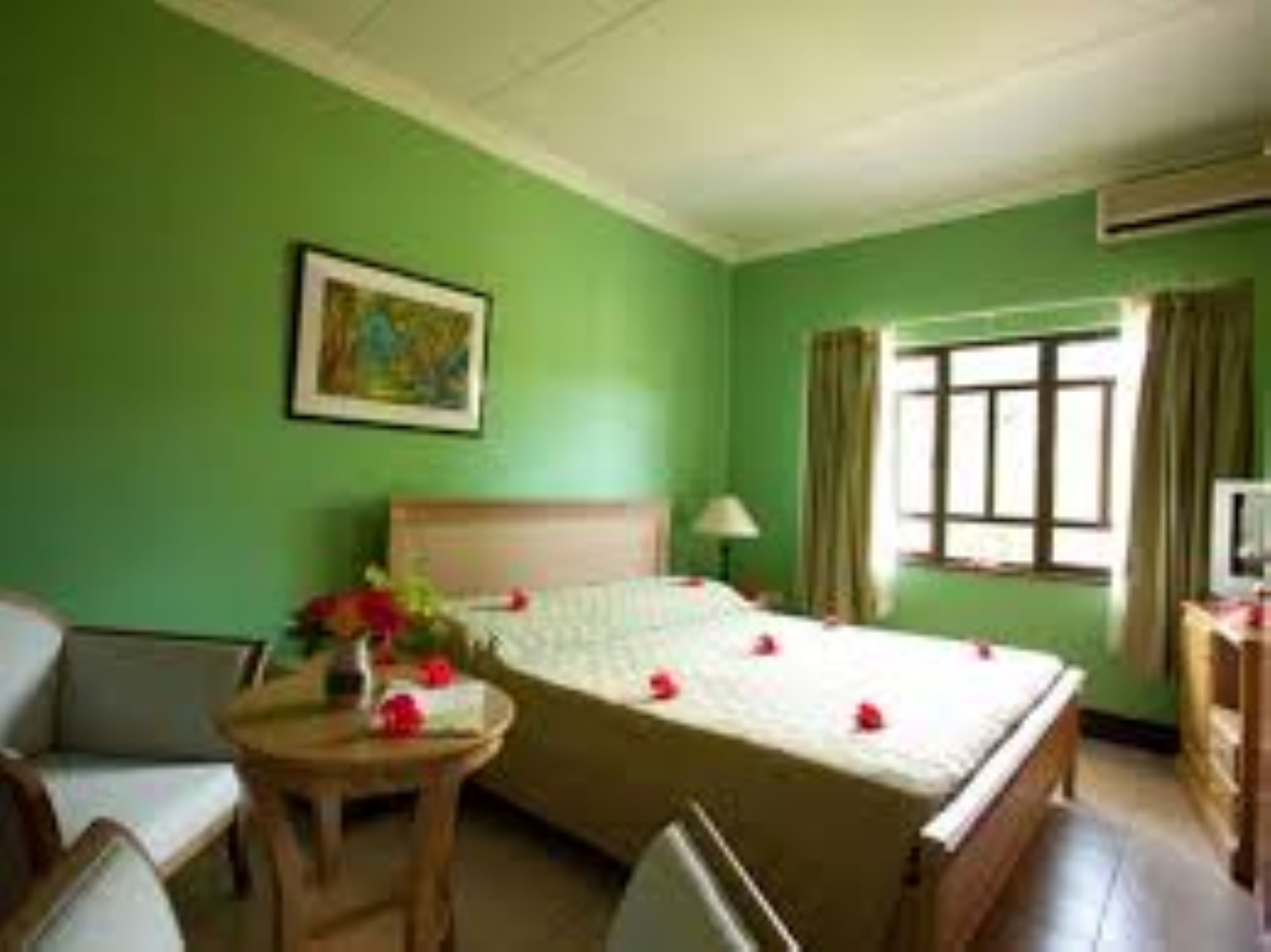 Ein Hotelzimmer mit einem Bett, einem kleinen Tisch mit Blumen in einer Vase, einem Sessel, einem Schreibtisch mit einer Lampe und einem Fernseher.