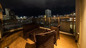 A balcony with wicker furniture and a view of the city at night. - Condominio Makishi Annesso (Naha)
