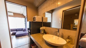 A compact bathroom with a sink, mirror, and two microwaves on the countertop. - Condominio Makishi Annesso (Naha)