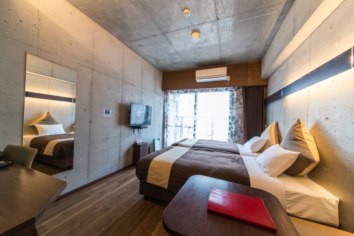 Une chambre d’hôtel avec un grand lit, un bureau, une chaise, une télévision et une fenêtre avec des rideaux.