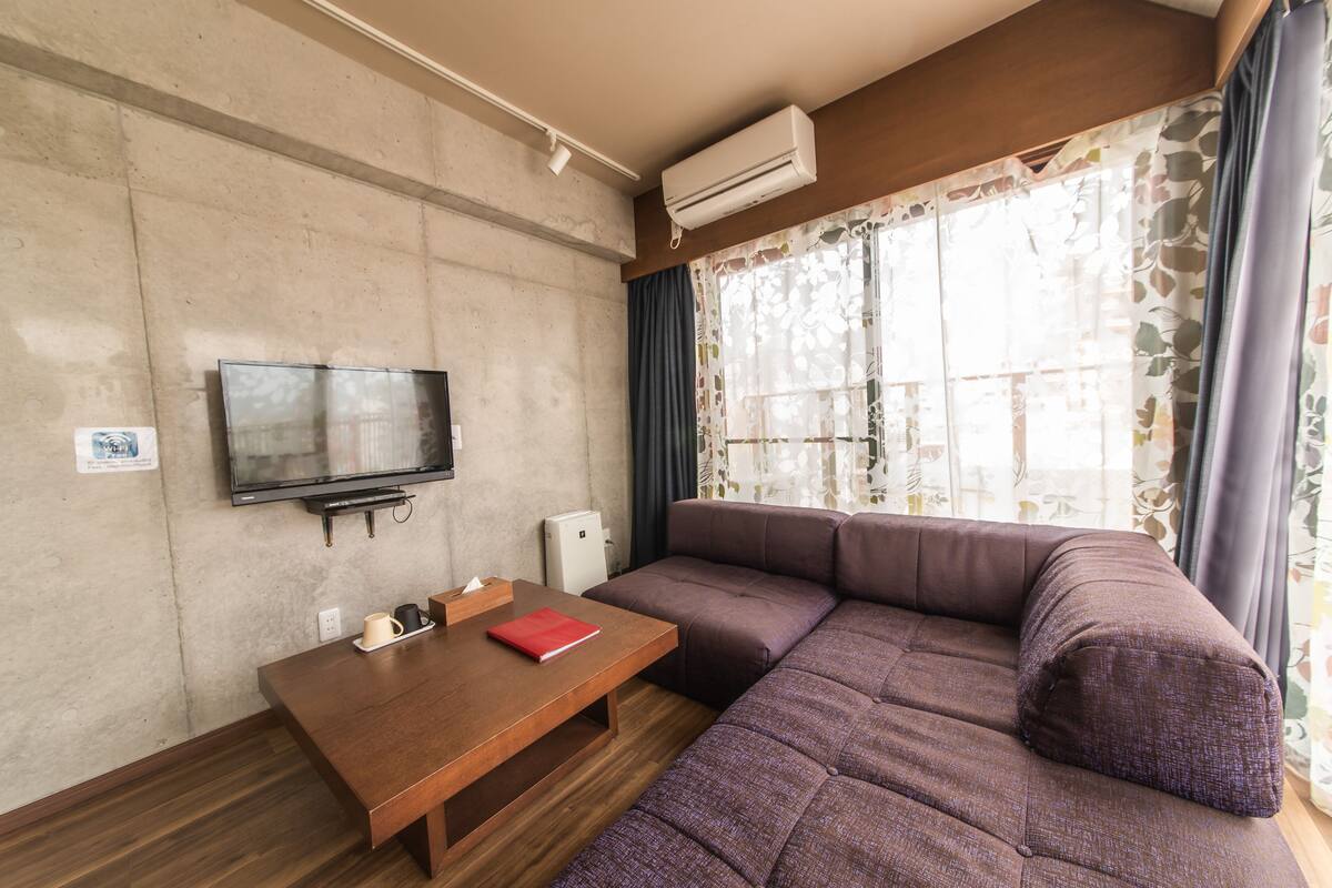 Un salon moderne avec une table en bois, un téléviseur à écran plat, un canapé et une fenêtre avec des rideaux.