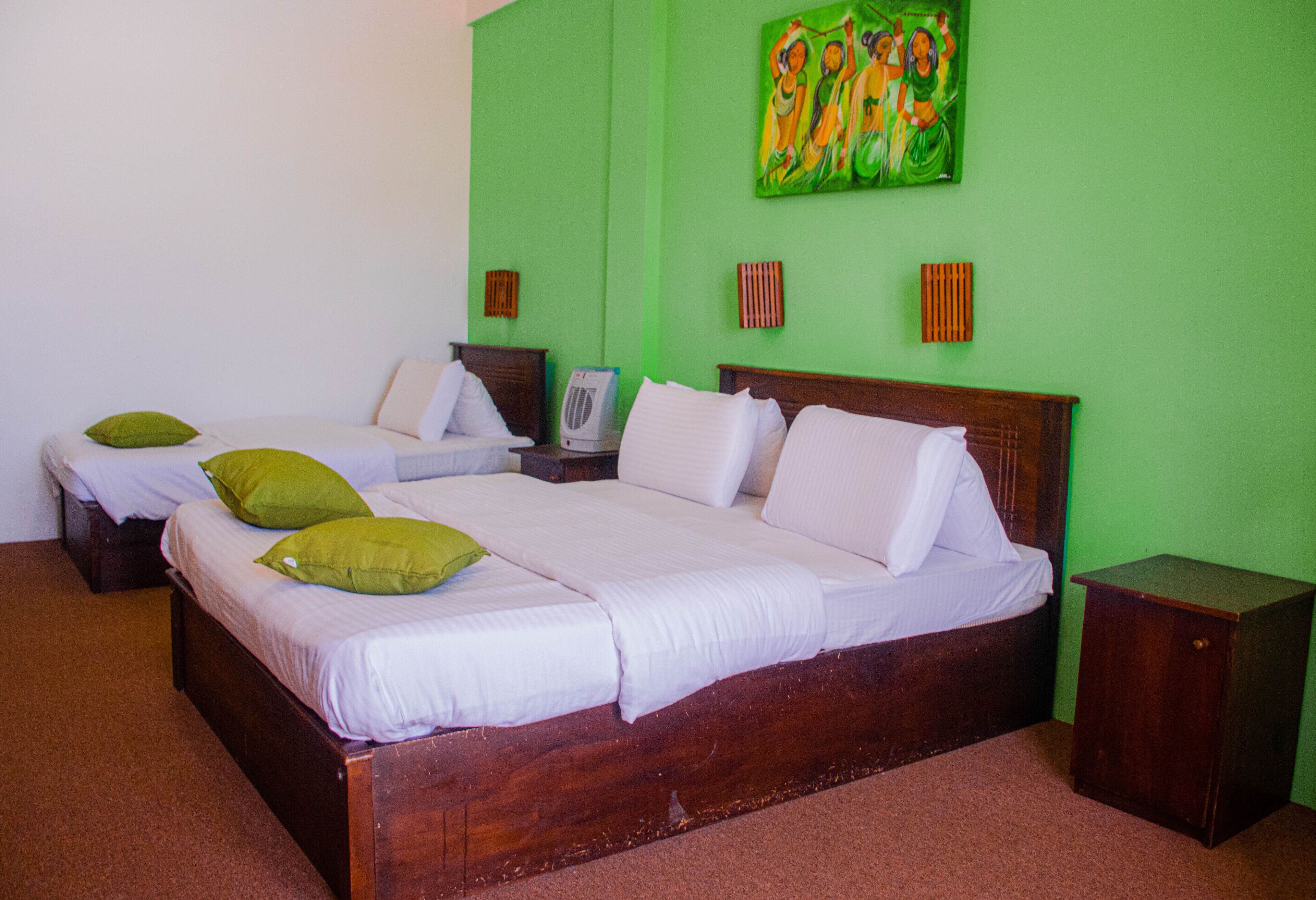 A hotel room with a large bed, two smaller beds, green walls, and a painting.