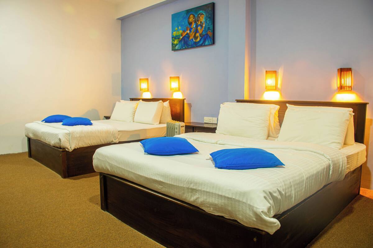 Habitación de hotel con dos camas, cada una con ropa de cama blanca y almohadas azules, y lámparas fijadas a la pared.