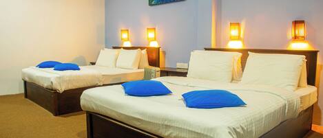 Habitación de hotel con dos camas, cada una con ropa de cama blanca y almohadas azules, y lámparas fijadas a la pared.