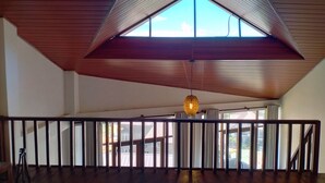 Une pièce spacieuse avec un plafond en pente, de grandes fenêtres et un luminaire suspendu.