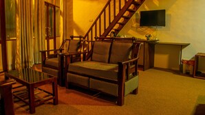 Un salon confortable avec un canapé, des fauteuils, une table basse, un téléviseur et un escalier.